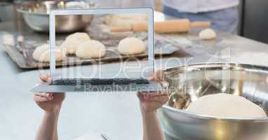 Hands holding laptop while photographing dough
