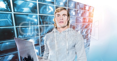 Shocked hacker holding laptop by screens