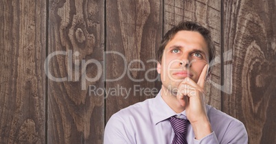 Thoughtful businessman with hand on chin against wooden wall