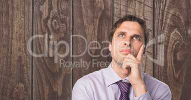 Thoughtful businessman with hand on chin against wooden wall