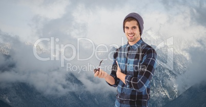 Male hipster holding smoking pipe against fog covering mountains