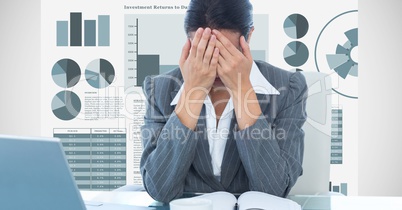 Stressed businesswoman covering face with hands against graphs