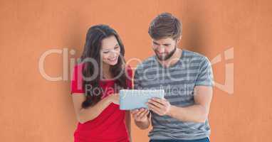 Male and female hipsters using digital tablet against orange background