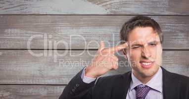 Portrait of businessman aiming forehead with finger against wooden wall