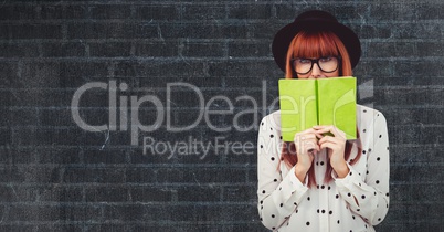 Female hipster covering face with book against wall