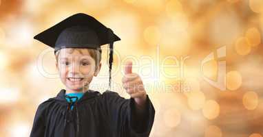 Portrait of happy boy in graduation gown and mortar board showing thumb up over bokeh