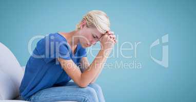 Woman sitting on couch with head on hands against blue background
