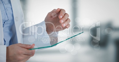 Doctor mid section with glass device behind bokeh against blurry grey office