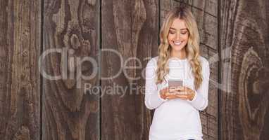 Happy woman using smart phone against wooden wall