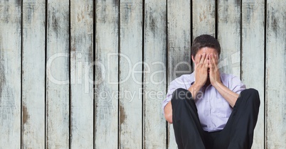 Depressed businessman covering face while sitting against wooden wall