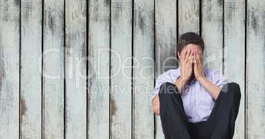 Depressed businessman covering face while sitting against wooden wall