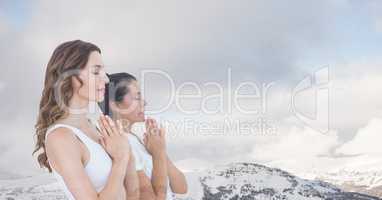 Double exposure of women with hands clasped meditating by snowcapped mountains