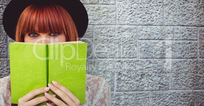 Redhead woman holding book in front of face against wall