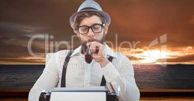 Male hipster with tobacco pipe looking at typewriter at beach during sunset