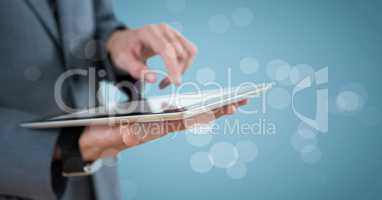 Business man mid section with tablet behind bokeh against blue background