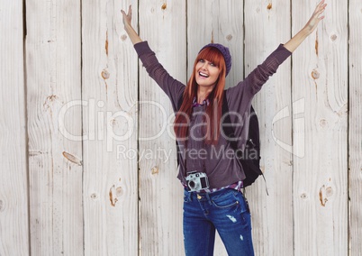 Female hipster with arms raised traveling against wooden wall