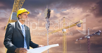 Architect holding blueprint against cranes