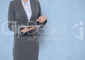 Midsection of businesswoman pointing at tablet PC over blue background
