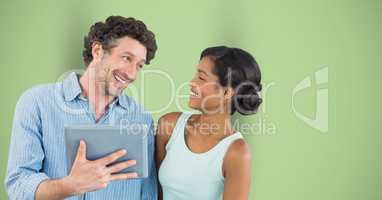 Happy businessman looking at female colleague while holding digital tablet against green background