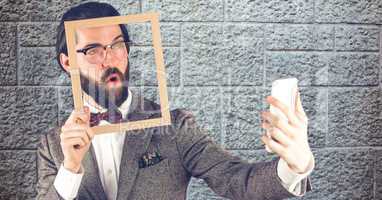 Hipster holding frame while taking selfie on smart phone
