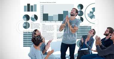 Business people applauding while looking at colleague with hands clasped against graphs