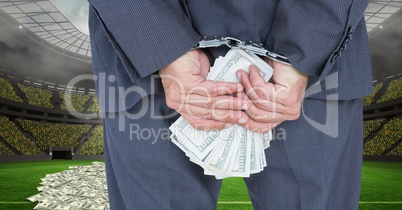 Midsection of businessman with handcuffs and money at football stadium representing corruption