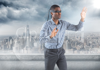 Business man blindfolded with flare against skyline and grey clouds