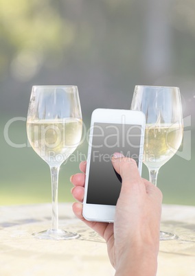 Hand holding phone with two glasses of champagne and sunny greenery