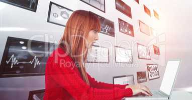 Female hacker using laptop against screens