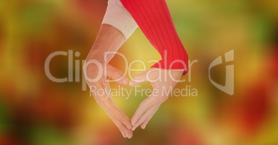 Cropped image of couple making heart shape with hands against bokeh