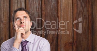 Thoughtful businessman with hand on chin against wood