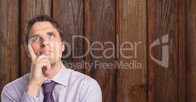 Thoughtful businessman with hand on chin against wood