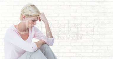 Woman sitting with head on hand against white brick wall