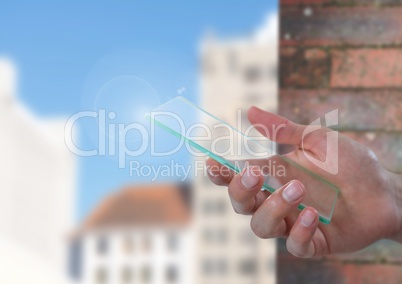 Hand holding glass screen with brick wall and buildings