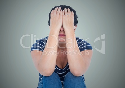 Woman sitting with hands on face against light blue background