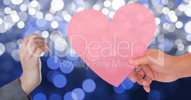 Hand giving pink heart shape to woman against bokeh