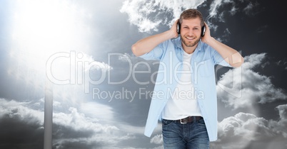 Smiling man listening to songs on headphones against sky