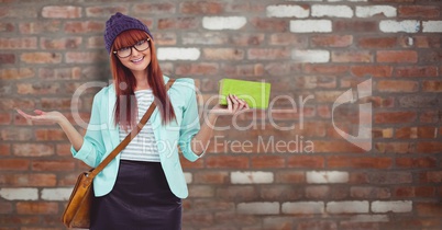 Hippie businesswoman holding clutch while gesturing against brick wall
