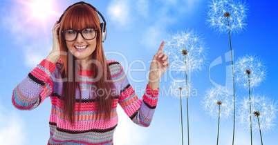 Redhead woman gesturing while using headphones by dandelions