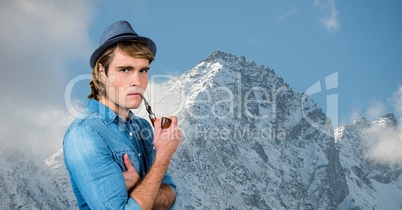Male hipster smoking pipe against snow covered mountains