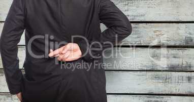 Midsection of businessman with fingers crossed against wooden wall