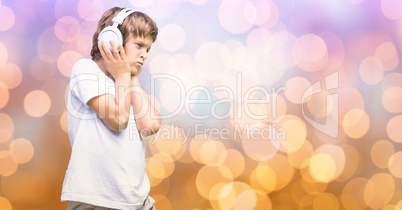 Boy listening music through headphones over bokeh