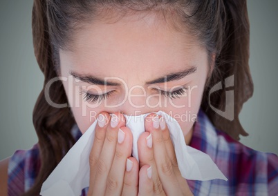 Close up of woman blowing nose against light blue background