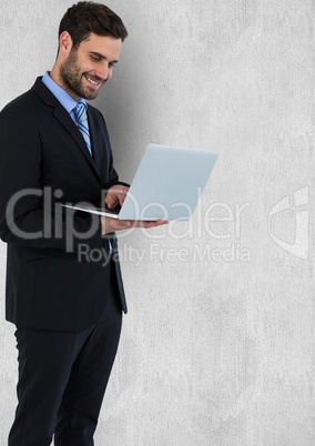 Businessman smiling while using laptop against wall