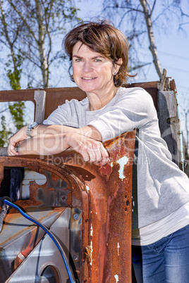 Woman stands in front of old scrap car