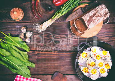 Fried eggs in a black frying pan, near bread and fresh vegetable