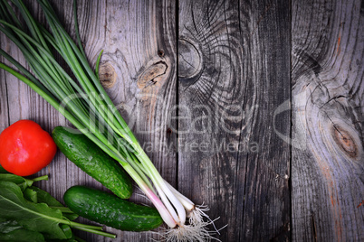 Green onions, tomato and cucumber on a gray wooden background