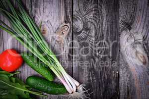 Green onions, tomato and cucumber on a gray wooden background