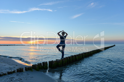 Frau macht Yoga im Sonnenuntergang am Meer