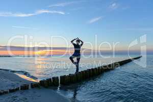Frau macht Yoga im Sonnenuntergang am Meer